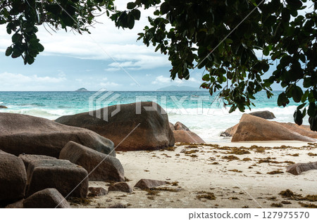 Massive granite boulders on a tropical beach of Praslin, Seychelles, with turquoise sea waves 127975570