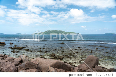 View of granite coastal rocks and ocean waves with distant islands on the horizon under cloudy View of granite coastal rocks and ocean waves with distant islands on the horizon under cloudy 127975581