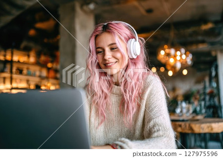 Young freelance woman with pink hair working on laptop in loft cafe with modern interior, concept of online work 127975596