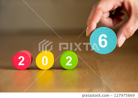Hand placing the number six to complete the year 2026 with colorful wooden cylinders Hand placing the number six to complete the year 2026 with colorful wooden cylinders 127975669