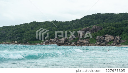 Granite cliffs and dense jungle meet the turquoise waves of La Digue island in Seychelles 127975805