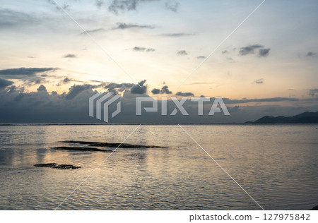 Cloud layers above calm sea reflect soft light at dusk near La Digue island, Seychelles 127975842