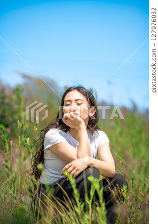 Young woman relaxing under blue sky 127976032
