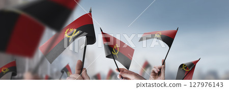 Angola flags in their hands on a blurred urban background 127976143