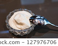 close up of cream in a flora transparent grand glass with a tea spoon, for adding to bread or coffee 127976706