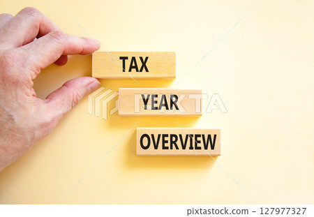 Tax year overview symbol. Concept words Tax year overview on beautiful wooden blocks. Beautiful white background. Businessman hand. Business tax year overview concept. Copy space. Tax year overview symbol. Concept words Tax year overview on beautiful wooden blocks. Beautiful white background. Businessman hand. Business tax year overview concept. Copy space. 127977327