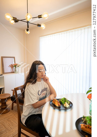 A young woman eating a meal while dressed casually indoors 127977412