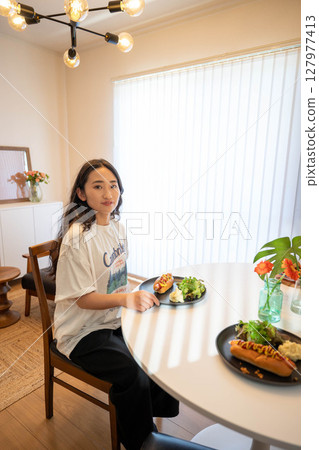 A young woman eating a meal while dressed casually indoors A young woman eating a meal while dressed casually indoors 127977413
