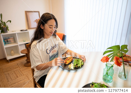A young woman eating a meal while dressed casually indoors A young woman eating a meal while dressed casually indoors 127977414