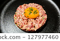 close up of raw egg and tuna tartar in a round shape on a black plate 127977460