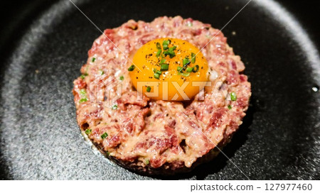 close up of raw egg and tuna tartar in a round shape on a black plate 127977460
