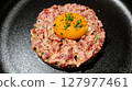 close up of raw egg and tuna tartar in a round shape on a black plate 127977461