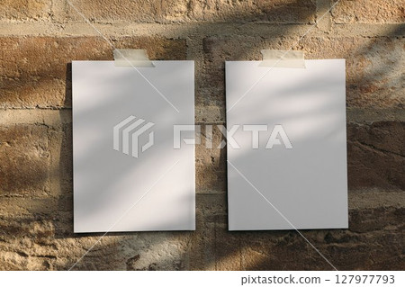 Two blank sheets of paper, greeting card templates taped to textured brick wall. Soft natural light and shadows overlay. Perfect mockup for design, artwork, message presentation. Summer modern setting 127977793