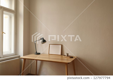 Minimalist workspace. Wooden desk, gray lamp, empty horizontal picture frame, poster mockup. Coffee cup on wooden tray by window. Modern Scandinavian interior, natural light. Home office setup. 127977794