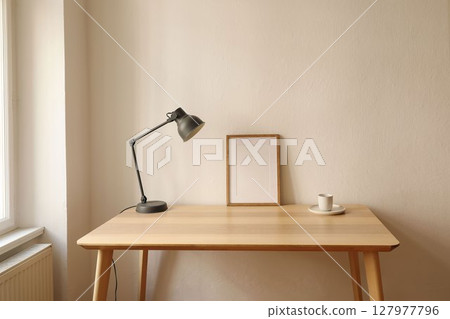 Elegant Scandinavian interior, living room. Blank thin wooden picture frame mockup on table near window. Modern lamp. Cup of coffee, tea. Trendy working space, home office. Beige wall background 127977796