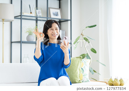A middle-aged housewife using a smartphone in the living room A middle-aged housewife using a smartphone in the living room 127977834