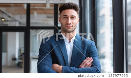 Confident Professional: Man in stylish blue suit, arms crossed, embodying success and modern professionalism. Eye contact, indoor setting. 127977933