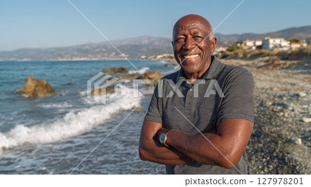 Smiling man at a rocky beach; a portrait of vitality and joy. He is standing confidently with arms crossed, showcasing a peaceful coastal scene. 127978201