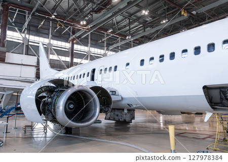 White passenger airliner in the airplane hangar. Aircraft under maintenance. Checking mechanical systems for flight operations White passenger airliner in the airplane hangar. Aircraft under maintenance. Checking mechanical systems for flight operations 127978384