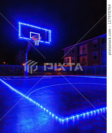Dark basketball arena with glowing blue lighting and central hoop 127978764