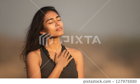 Serene Woman Meditating Outdoors, a moment of mindfulness and peace. With eyes closed and hand to chest, she embodies tranquility and inner harmony in nature. Serene Woman Meditating Outdoors, a moment of mindfulness and peace. With eyes closed and hand to chest, she embodies tranquility and inner harmony in nature. 127978880