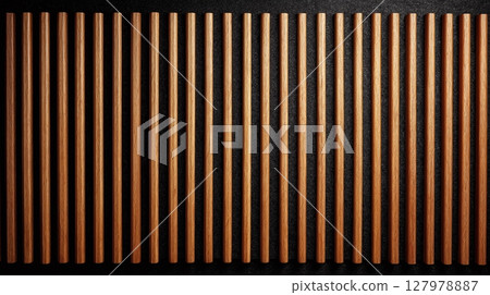 A dark background is covered by evenly spaced light brown wooden rods, creating a structured and textured design. 127978887