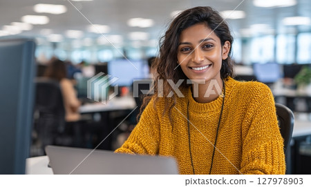 Smiling young woman working in open office. Happy, confident worker in a yellow sweater. Friendly office environment. Positive work vibes. 127978903