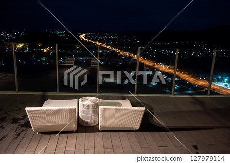 bed chairs on hotel rooftop with Hua Hin city view at night 127979114