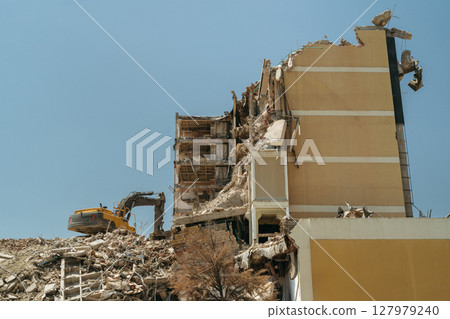 Demolition site with a collapsed building, exposed rebar, and a bulldozer Demolition site with a collapsed building, exposed rebar, and a bulldozer 127979240