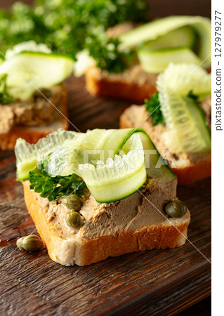 Open sandwiches with pate, cucumber, capers, and parsley on a old cutting board. 127979277
