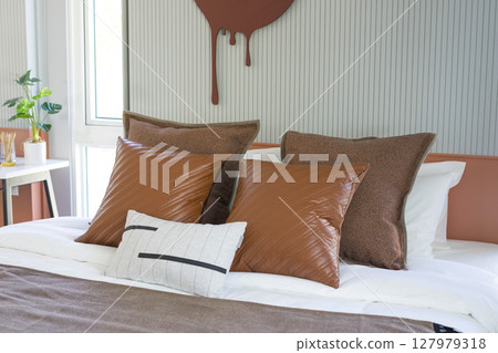Modern stylish bedroom with brown and leather pillows setting. Large art piece on wall. 127979318