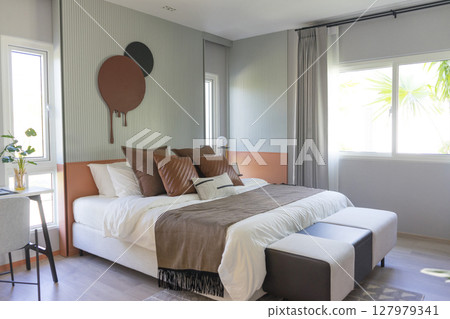 Comfortable bed with brown stylish linens and pillow with painting on wall. Interior design. 127979341