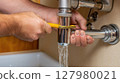 Hand repairing a leaking pipe under the kitchen sink 127980021