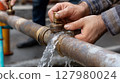 Hand repairing a water pipe with flowing water in an outdoor 127980024
