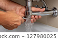 Hand repairs a leaking pipe under the sink 127980025