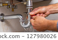 Hand performing pipe repair under kitchen sink during home maintenance task 127980026