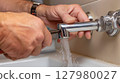 Hands repairing a leaking pipe under the sink 127980027