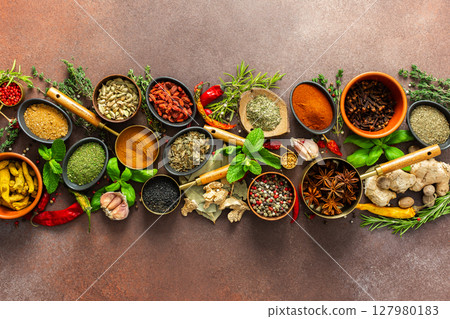 A stunning spread of fresh spices and herbs, meticulously arranged on a deep brown backdrop, capturing their vibrant colors and tantalizing aromas 127980183