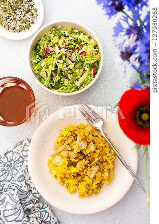 Stewed rice with chicken breast and mixed salad with radishes and various seeds, a served table with food and a vase of flowers Stewed rice with chicken breast and mixed salad with radishes and various seeds, a served table with food and a vase of flowers 127980268