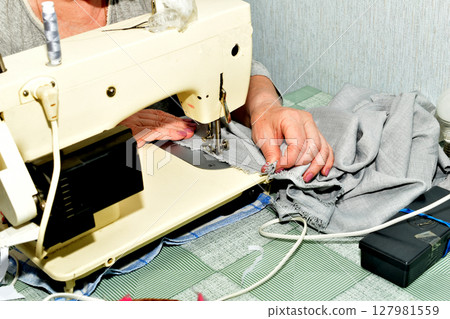 The seamstress sews on a sewing machine. The seamstress sews on a sewing machine. 127981559