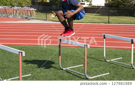 Athlete Jumps Over Hurdles on a Training Field Athlete Jumps Over Hurdles on a Training Field 127981989