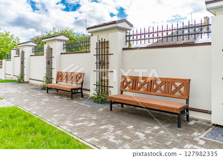 Back and front yard cottage garden, flowering plant and green grass lawn, brown pavement and orange brick wall, evergreen trees on background, in good care maintenance landscaping in park 127982335