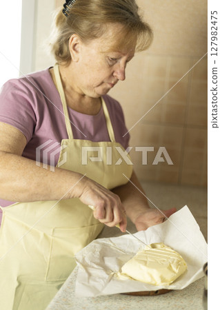 senior woman is slicing sweet cream butter into chunks senior woman is slicing sweet cream butter into chunks 127982475
