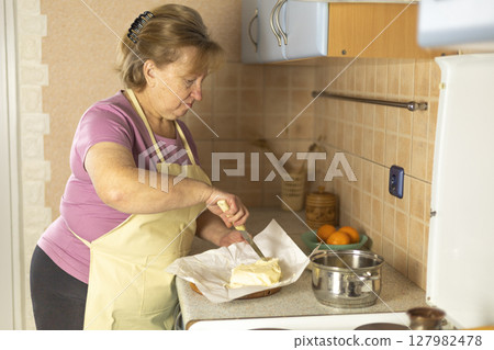 A senior woman chops sweet butter into pieces. 127982478