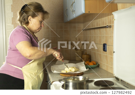 Senior woman in an apron preparing sweet butter for heating on an electric stove, preparing ghee butter Senior woman in an apron preparing sweet butter for heating on an electric stove, preparing ghee butter 127982492