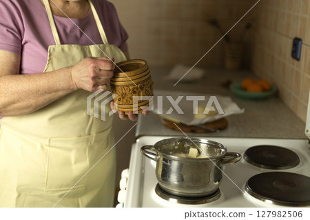 The hands of a senior woman add salt to sweet butter on the stove 127982506