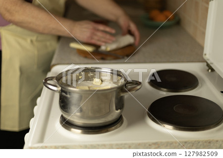 semi-melted butter in a saucepan on the stove, in the background the hands of a senior woman semi-melted butter in a saucepan on the stove, in the background the hands of a senior woman 127982509
