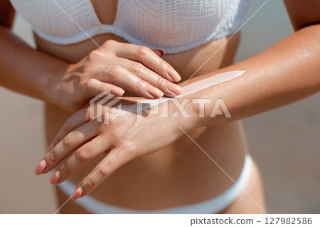 Hand of a young woman applying sun cream or sunscreen on her tanned arm to protect her skin from the sun.  Skincare. Body Sun protection lotion. 127982586