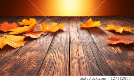 Autumn leaves scattered on wooden floor with warm orange glow 127982963
