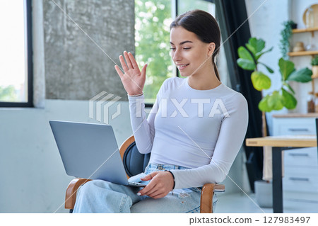 Young teenage girl using laptop for video chat sitting on chair at home Young teenage girl using laptop for video chat sitting on chair at home 127983497